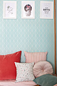 Colourful decorative cushions in front of light blue diamond-shaped wallpaper with white picture frames