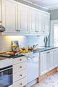 Bright country-style kitchen with white wooden fronts and fresh pastries on the worktop