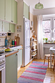 Kitchen with pastel green cupboards and colourful carpet runner