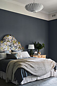 Bed with floral headboard in front of a dark blue wall in the bedroom