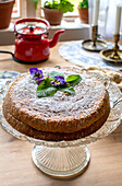 Homemade cake with icing sugar and violets on a glass cake plate