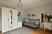Guest room with metal bed, white wardrobe and light grey wall