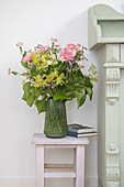 Green glass vase with a bouquet of summer flowers on a stool