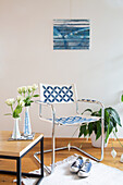 White and blue cantilever chair with graphic pattern, wooden and metal table, white vase with roses