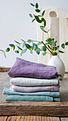 Folded linen cloths in pastel colours next to vase with eucalyptus