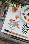 Painting utensils and watercolour painting of sparrow with marigold flowers on wooden table