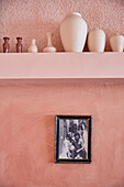 Pink wall with shelf full of vases above framed black and white photo