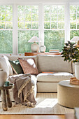 Bright living room with beige corner sofa, round tables and large windows