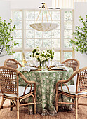 Round dining table with green patterned tablecloth and rattan chairs in front of a large window