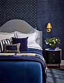 Blue bedroom with patterned headboard and golden wall lamp