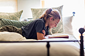 Dreizehnjähriges Mädchen liegt auf dem Bett und liest beim Tageslicht