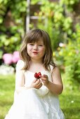 A little girl eating a strawberry in a garden