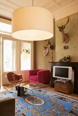 Wohnraum im Stilmix mit Designerstuhl, Polstersessel, Jagdtrophäen, Seidenteppich und Hängelampe im Sixtiesstil