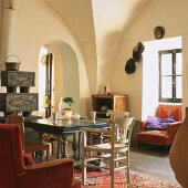 Wohnzimmer mit Deckengewölbe, Kaminofen, Durchgang mit Rundbogen, antikem Holztisch und goldbestickten Polstersesseln