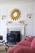 Wood-burner and magnificent mirror with gilt sunburst frame on wood-panelled white wall