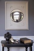 Animal horns and antique book on black console table below convex mirror
