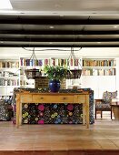 Schlichter Holztisch mit Blumenvase hinter der Couch im Wohnzimmer mit Terrakottafliesen und ausladender, weisser Bücherwand