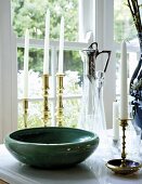Green bowl and shiny candlestick on table in front of window