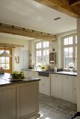 Sonnige Küche mit schweren Deckenbalken, Terrakottafliesen am Boden und weiße Holzschränke