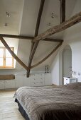 Schlafzimmer mit Holzdielenboden und einem Doppelbett unter rustikalen Dachbalken