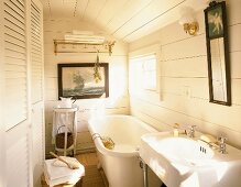 Small bathroom with white wooden walls, fitted cupboard with louver doors, large bathtub and maritime picture on wall