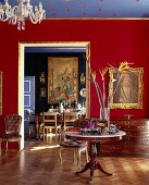 Goldgerahmter Raum mit rundem Tisch mit Marmorplatte, einem Papageienblumenstrauss und mit Blick in ein opulentes Esszimmer mit großem Wandbehang