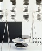 Black and white arrangement of small table with three levels, two designer standard lamps and patterned wallpaper