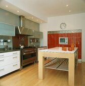 Ein massiver Küchentisch steht in der Mitte der modernen Küche mit Edelstahlelementen und rotem Einbauschrank