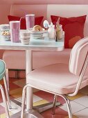 Quadratischer Metalltisch in einem Diner; dazu eine rosafarbene Sitzbank und passenden pastellfarbenen Stühlen