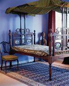Antikes, marrokkanisches Baldachinbett auf einem alten Orientteppich, daneben ein barocker Stuhl