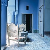 Weissgold gestrichene, niedrige Holzstühle und ein gedeckter Kaffeetisch im blauen Arkadengang eines orientalischen Wohnhauses