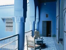 Ein Kaffeetisch mit Holzstühlen im Arkadengang eines blau gestrichenen, typisch orientalischen Wohnhauses
