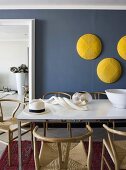 Gelbe Dekoscheiben an der blauen Wand des Esszimmers mit minimalistischem Esstisch und gebogenen Holzstühlen