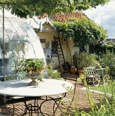 Romantische, sonnige Landhausterrasse mit Steinboden und rundem Gartentisch
