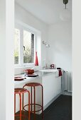 Rote Barhocker an einer weissen Küchenzeile mit Edelstahloberfläche