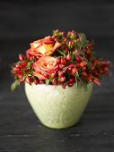 Arrangement of rose hips and roses in green pot