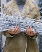 Woman holding white branches (Christmas decorations) outside house