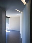 Blick durch offenen Durchgang in leeren Raum mit eingelassenen Deckenlichtbändern einer modernen Architektur