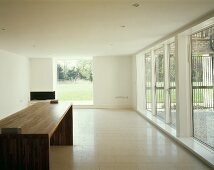Moderner leerer Wohnraum mit Designer Tisch aus Holz und raumhohen Fenstern mit Gartenblick