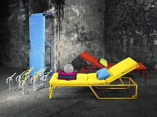 Coloured loungers arranged in front of a weathered, grey stone wall