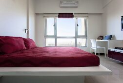 Rotbezogenes Doppelbett in weißem Schlafzimmer mit grossem Fenster