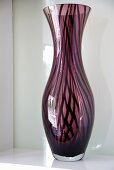 A purple striped vase in front of a white glass panel