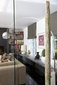 A stainless steel hanging floor lamp in a living room with a shelf under the windows