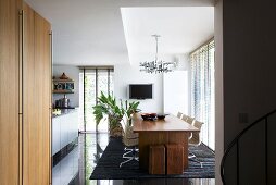 A view into a dining room with a wooden table, designer chairs and shiny black floor tiles