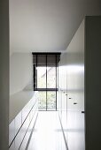 Schmaler Raum mit weißem Sideboard und weißem Hochschrank an den Längsseiten, ein raumhohes Fenster stirnseitig