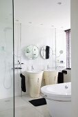 A white bathroom with a free-standing basin and a unit underneath it, a round mirror on the wall and black towels
