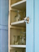 A metal door knob on a blue cupboard with an open door