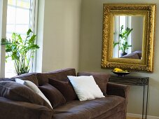 A brown upholstered sofa and a mirror with a gold frame in a the corner of a living room