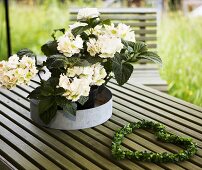 White flowers in a metal dish and a heart-shaped wreath of leaves on a garden table