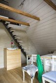 Stuhl und Treppe unter Dachschräge mit weisser Holzverkleidung und Holzbalken